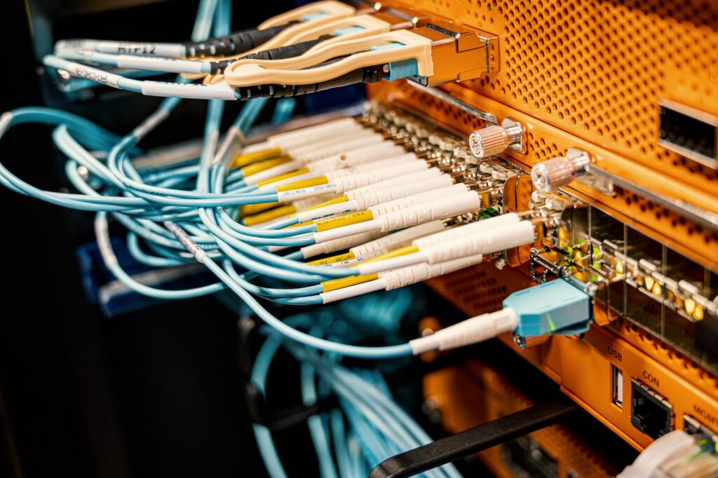 Teal fibre patch cords and white-labelled cables running into an orange rack chassis