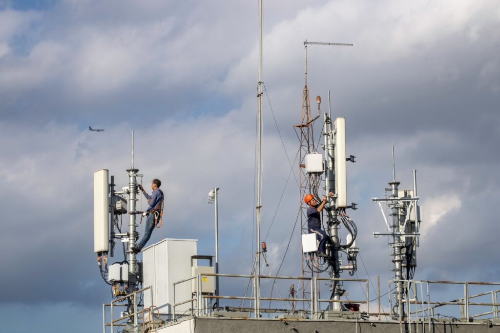 Two technicians in harnesses working on cellular antennas at a rooftop cell site