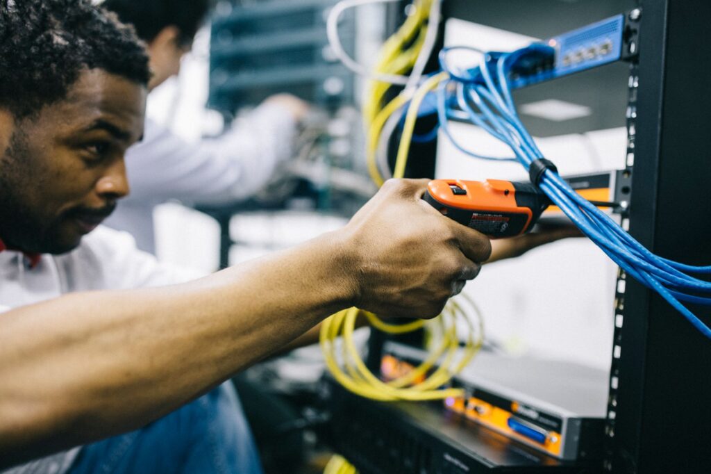 A technician uses a screwdriver on equipment mounted in an open network rack