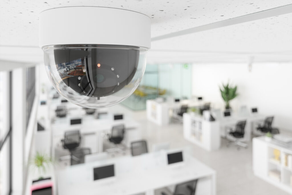 A dome security camera mounted on the ceiling above an open-plan office